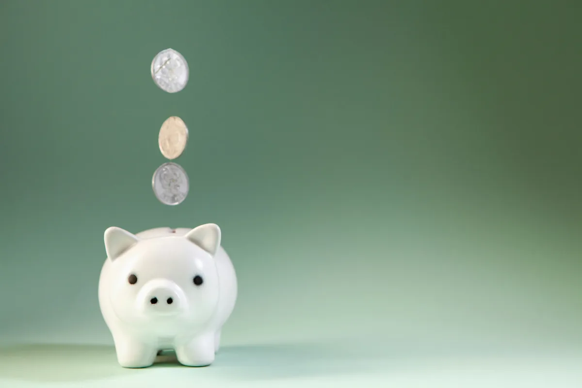 Coins falling into a white piggy bank.